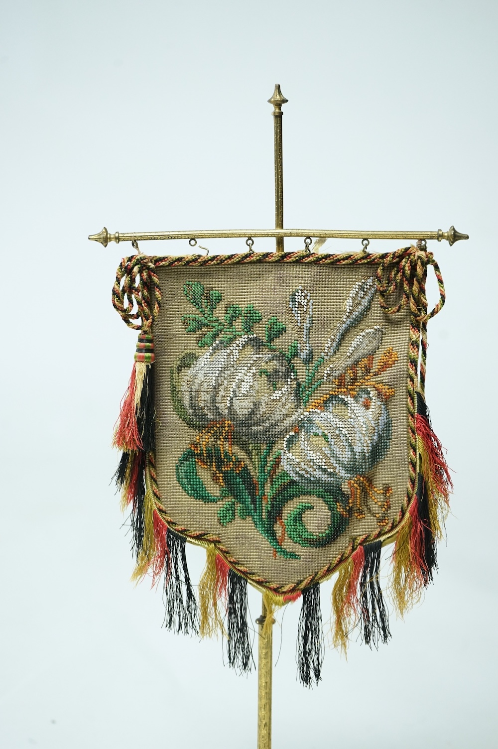 A pair of 19th century cast brass table screens, with floral Berlin Bead worked banners. 54cm high. Condition - the fringing has worn in places, silk backing has torn, both could be removed.